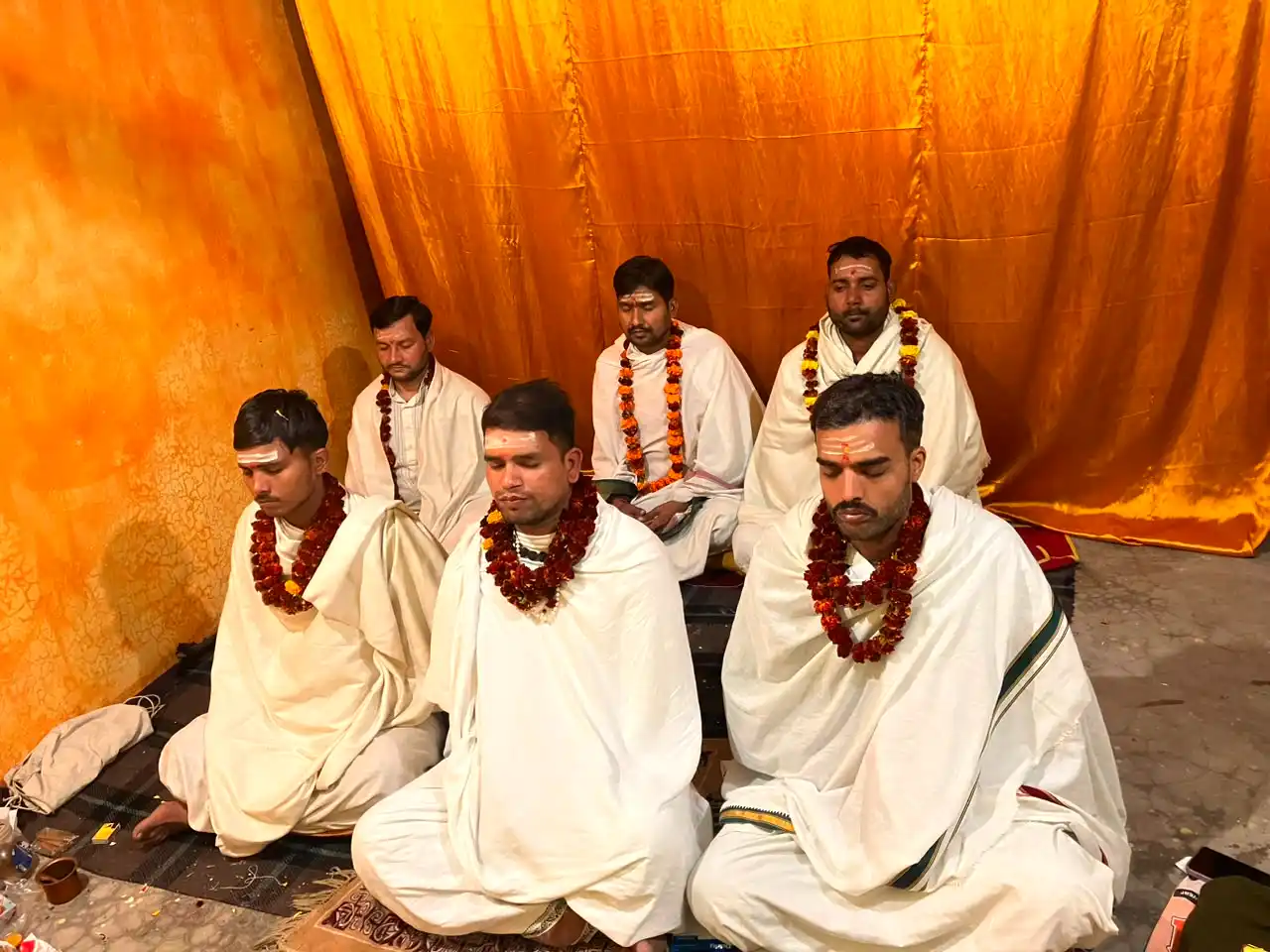Priests wearing marigold garlands in quiet meditative reflection